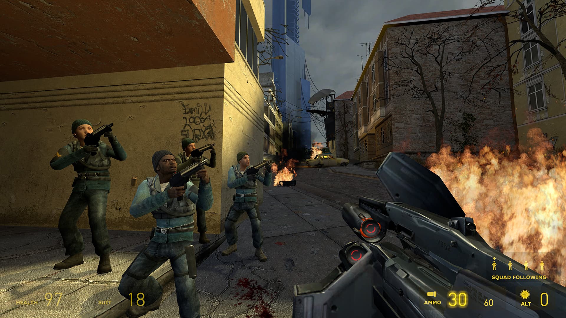 A screenshot from Half-Life 2. A squad of rebels aims at the skies as Gordon Freeman watches amidst burning wreckage in the war-torn streets of City 17.