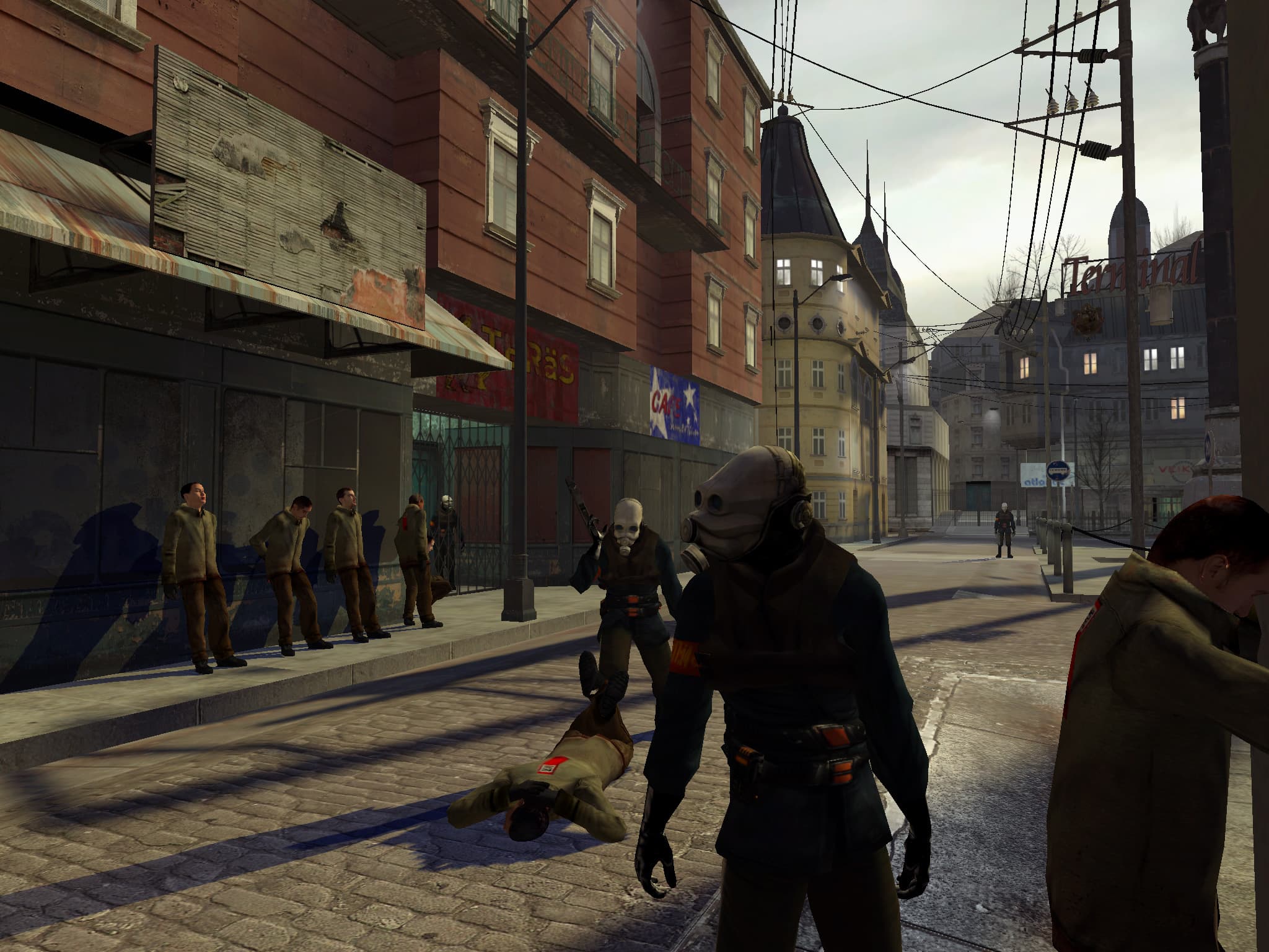 Two metro cops hold one citizen against the wall and another to the floor while four other citizens stand against a wall. An Eastern European plaza can be seen in the background, with a terminal sign above a building in the distance.